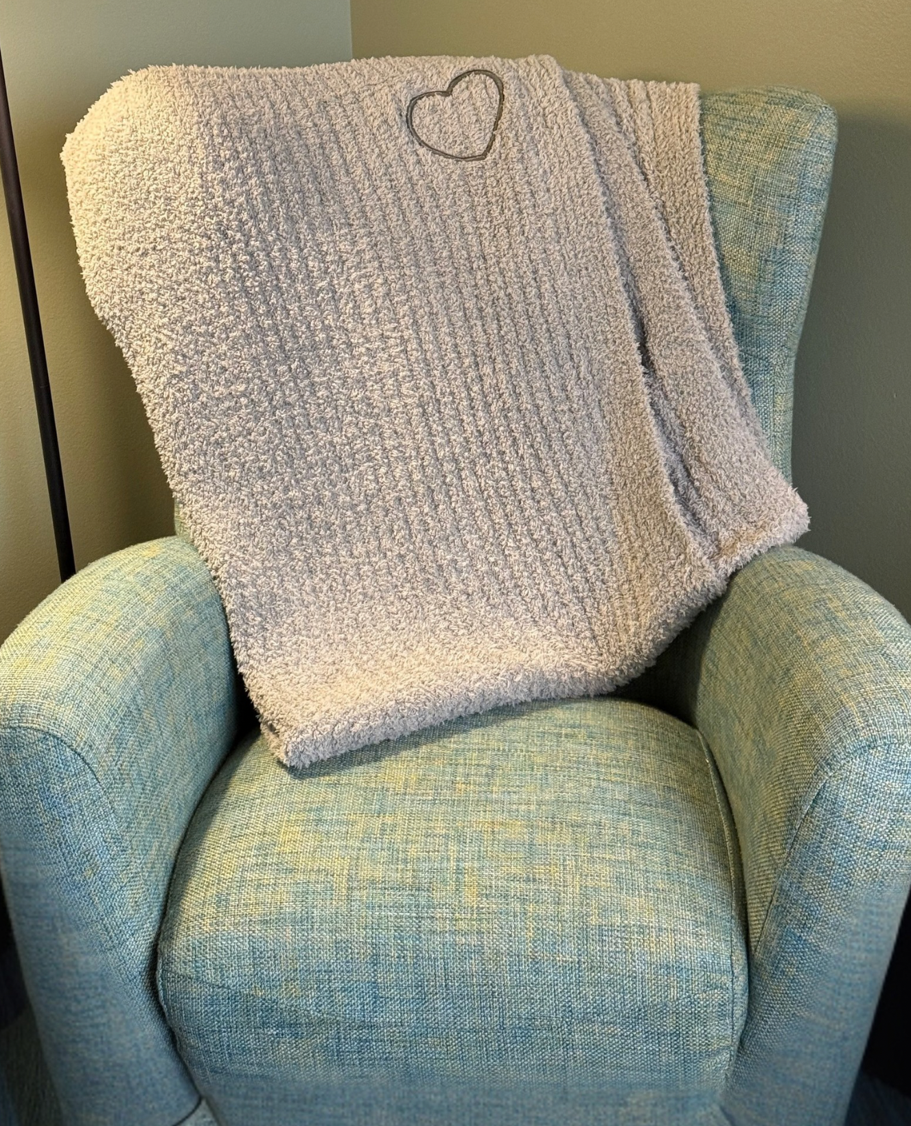 Ocean Mist chenille comfort blanket draped over a chair, featuring the signature embroidered heart detail.
